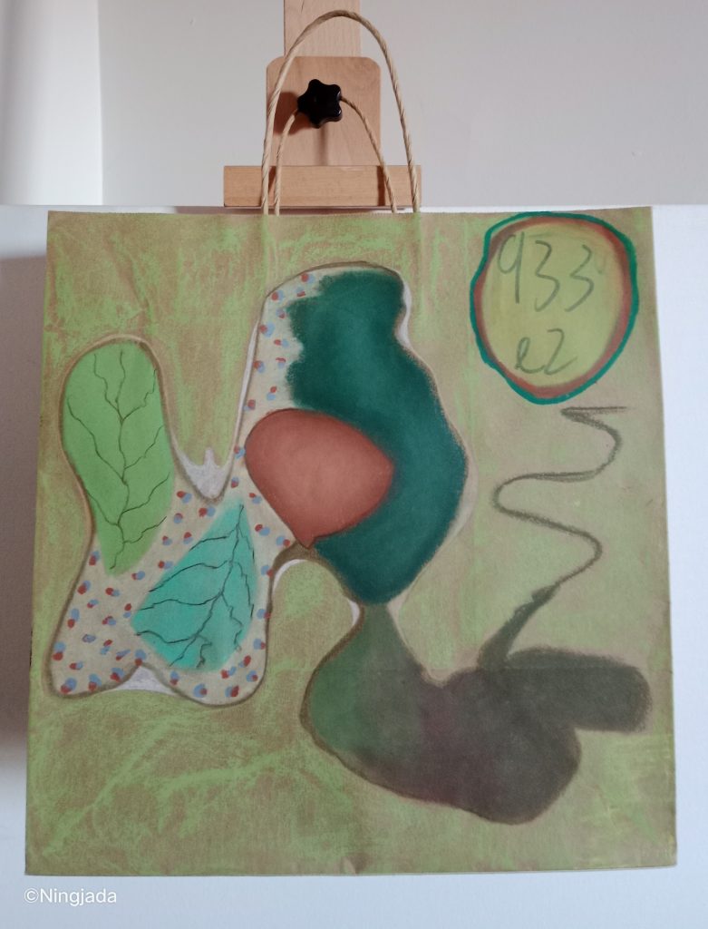 Image is a photo of a brown paper bag which has been drawn on, hanging on a wooden easel, in front of a white wall. The bag is coloured with a thin coat of green oil pastel, parts of the brown bag is still visible. The centre of the bag has an oblong shape with a brown outline, inside the shape is a painted green leaf, teal leaf, dark red oval shape, sporadic blue and red connected dots and dark teal and dark green shaded areas. The top right of the bag has a drawn circle with “933 e2” written in dark green. The circle is outlined by a red and green line.