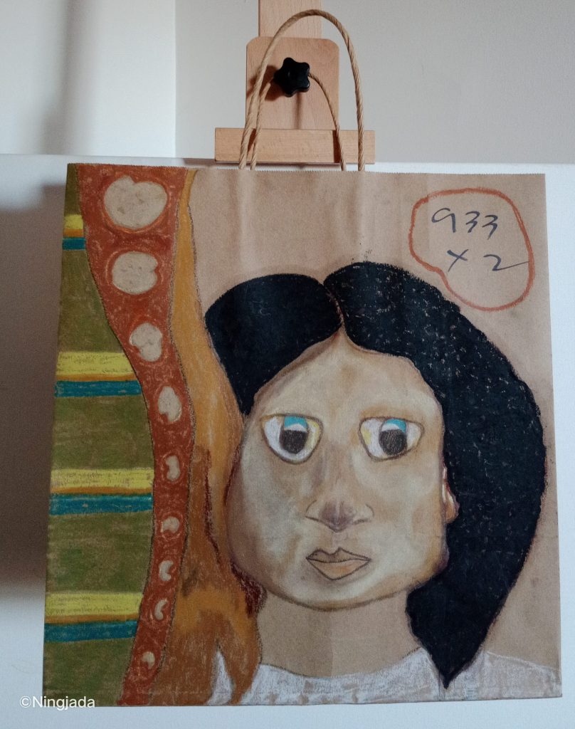 Image is a photo of a brown paper bag which has been drawn on, hanging on a wooden easel, in front of a white wall. A womans face has been drawn centre of the bag. Their skin is pale, eyes are blue, they have black hair down to the shoulder and are wearing a collarless white top. The left side of the bag is an obscure drawing. It has three sections ,dark green with vertical yellow, orange and blue striped pattern. Red background with circles, this section starts wider then becomes thin from top to bottom, the third section is an orange flame shape, connected to the red section, the left side of the woman’s face is against it. “933x2” is circled in red at the top right of the bag.
