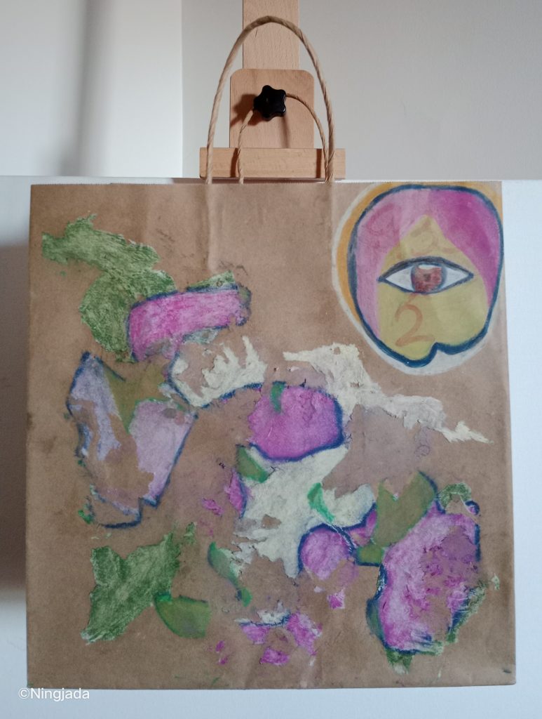 Image is a photo of a brown paper bag with a drawing on it, hanging on a wooden easel, in front of a white wall. The centre of the bag is covered in a floral like pattern with green, white and lilac colours outlined with dark purple. In the top right of the bag is a circle with a dark red eye in the centre and pink and yellow shades surround it. The number “933 2” is faded in red behind the circle.