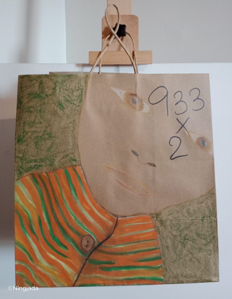 A brown paper bag has a picture drawn on it. The top right of the bag is a pale brown face, with brown eyes. The head is diagonally tilted with the top of the head in the top right corner. The upper torso of the person is wearing a bright orange buttoned top, with horizontal zebra stripes of yellow and green shades. The background behind the person is a dark grassy green. The number “933x2” is drawn over the persons forehead .The paper bag is hung up on a wooden easel.