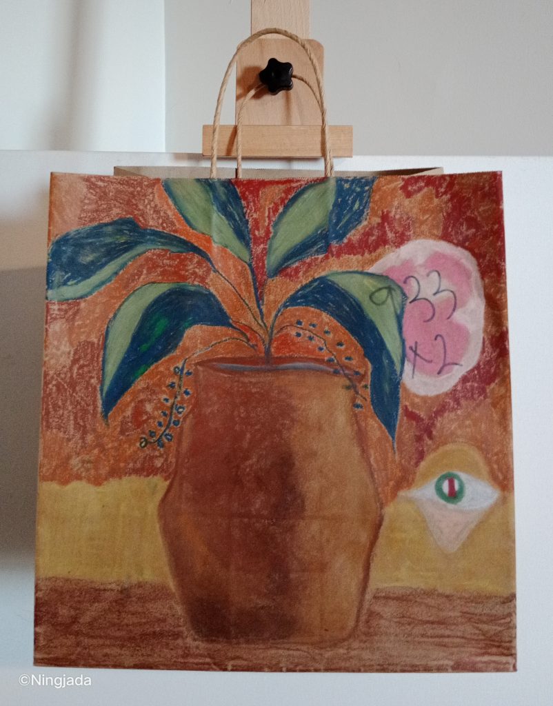 A brown bag has a vase with a plant drawn on it. The vase is a terracotta colour and is shaded darker on the left side. The plant has five leaves, which are all half light green and dark blue. The plant has two small vines which are fruiting small blue dots. The vase is on a dark brown surface at the bottom of the bag. In the background above the brown surface is a thin mustard yellow section. On the right side of this section is a green eye with a red and white pupil. The skin under the eye is a pale cream colour, the eyelid is mustard yellow. The rest of the background above the eye and the mustard yellow section is an orange and red shaded section. The top right of the bag has the number “933x2” written in thin black pen and is in a pink shaded circle with a white outline. The bag is hanging on a wooden easel in front of a white wall.