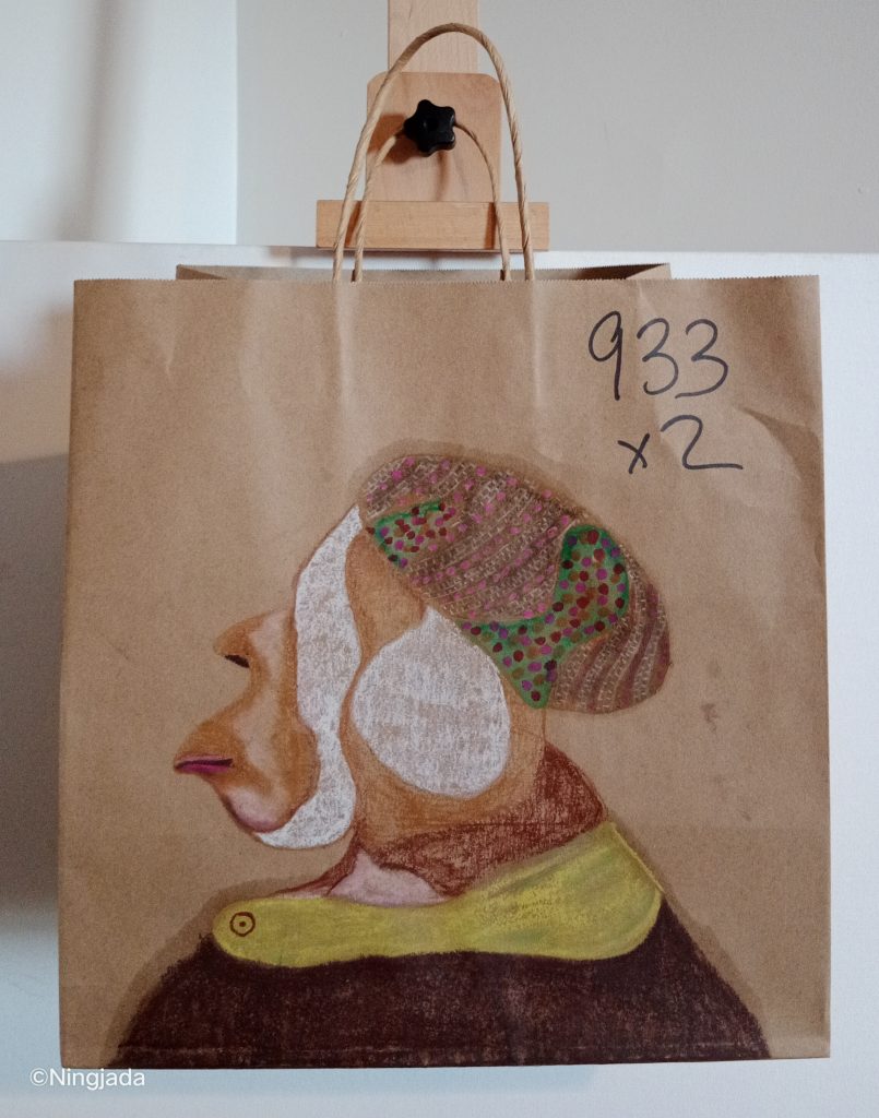 A brown paper bag has a side profile of a person drawn on it. The profile is faced to the left, the person is wearing a round hat. The hat is patterned with different coloured dots of purple, pink, white, red and green. The person has a white circle covering their ear, and also a white stripe from their forehead down to under their jaw covering over their eyes and cheek. The persons nose and lips are quite pronounced. The person is wearing a red collared shirt with a coat over the top. The coat is black with a large lime green collar. The background is not coloured in, and “933x2” is written in think black pen at the top right of the bag. The bag is hanging on a wooden easel, in front of a white wall.